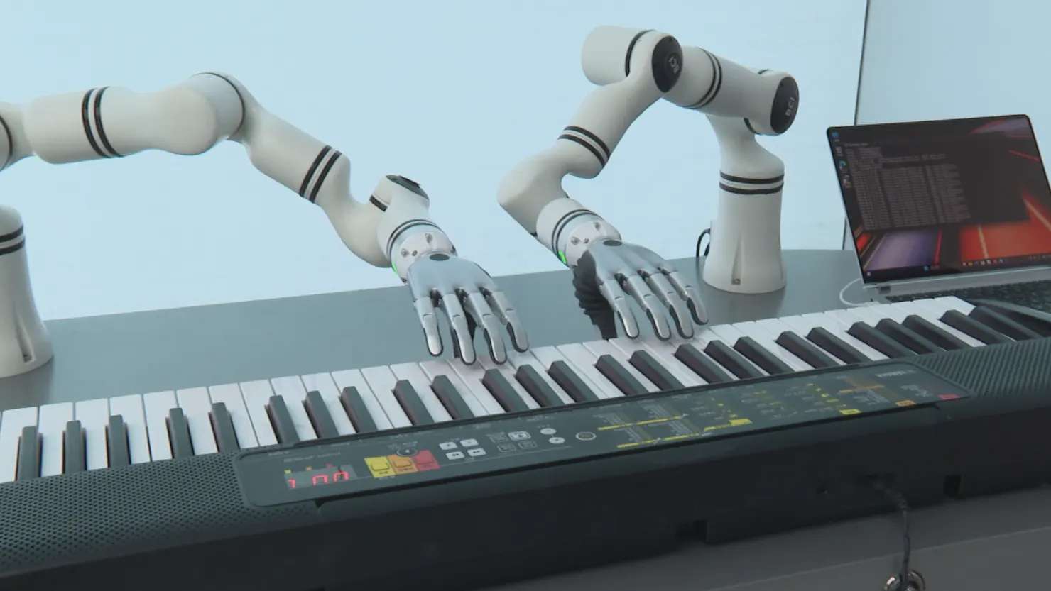 Deux bras robotiques équipés de mains artificielles jouent sur un clavier de piano.