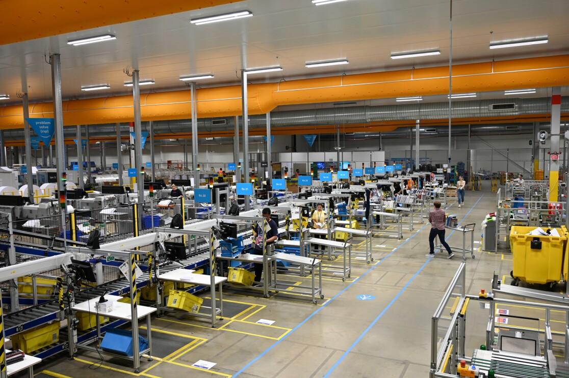 Vue intérieure d’une grande installation Amazon avec postes de travail, convoyeurs et équipements industriels