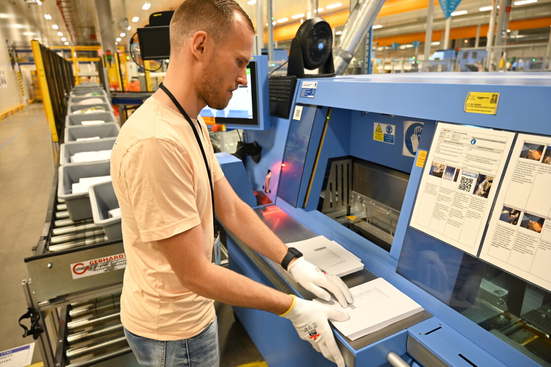 Employé manipulant des piles de livres devant une grande machine industrielle dans une installation Amazon