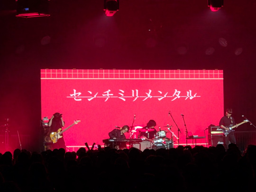 Centimillimental et ses musiciens sur une scène éclairée en rouge devant le public d’Otakuthon 2026.