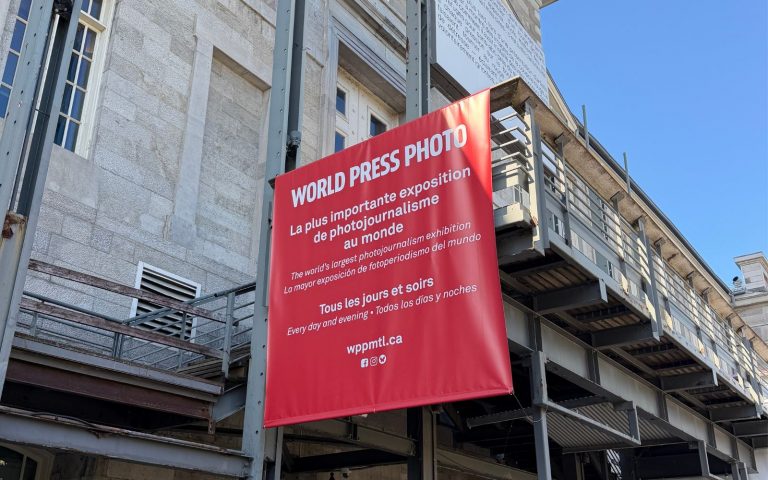 Bannière rouge de l’exposition World Press Photo accrochée à la façade d’un édifice en pierre, sous un ciel bleu