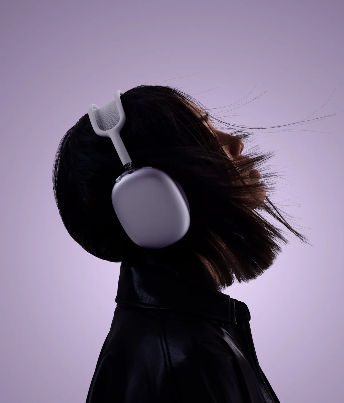 Femme de profil portant un casque AirPods Max mauve, cheveux au vent, sur fond lilas