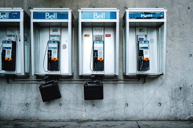 Rangée d'anciens téléphones publics Bell installés dans des cabines métalliques contre un mur de béton.