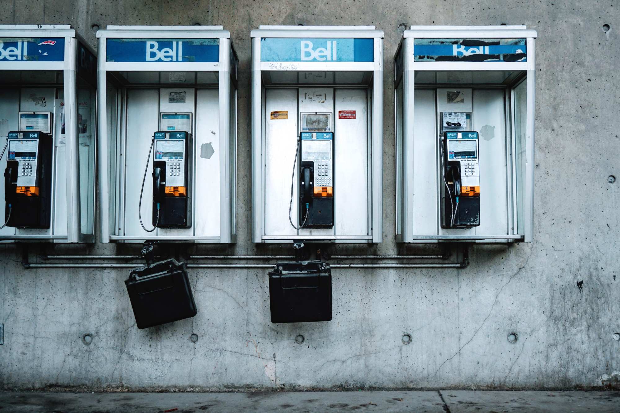Rangée d'anciens téléphones publics Bell installés dans des cabines métalliques contre un mur de béton.