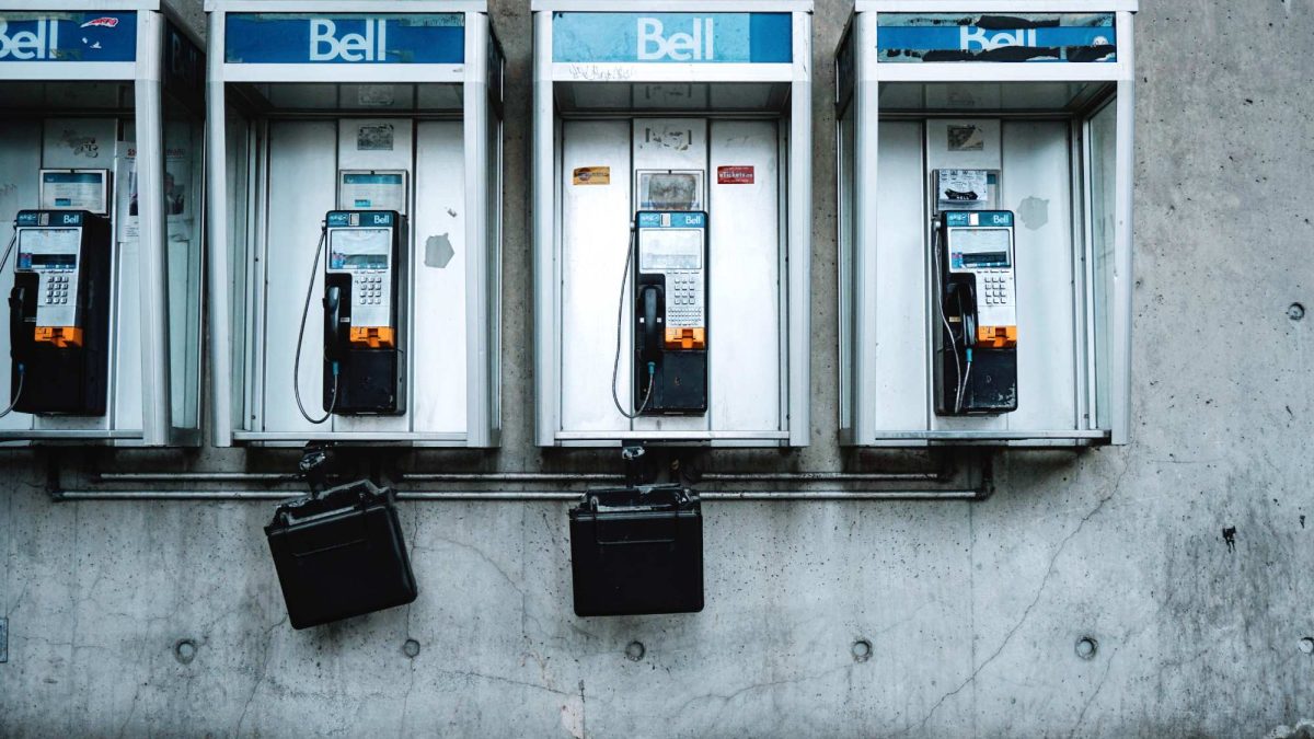 Rangée d'anciens téléphones publics Bell installés dans des cabines métalliques contre un mur de béton.